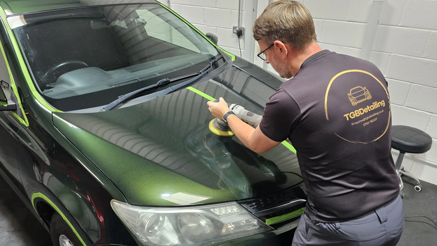 Machine polishing a dark green car with trim masked